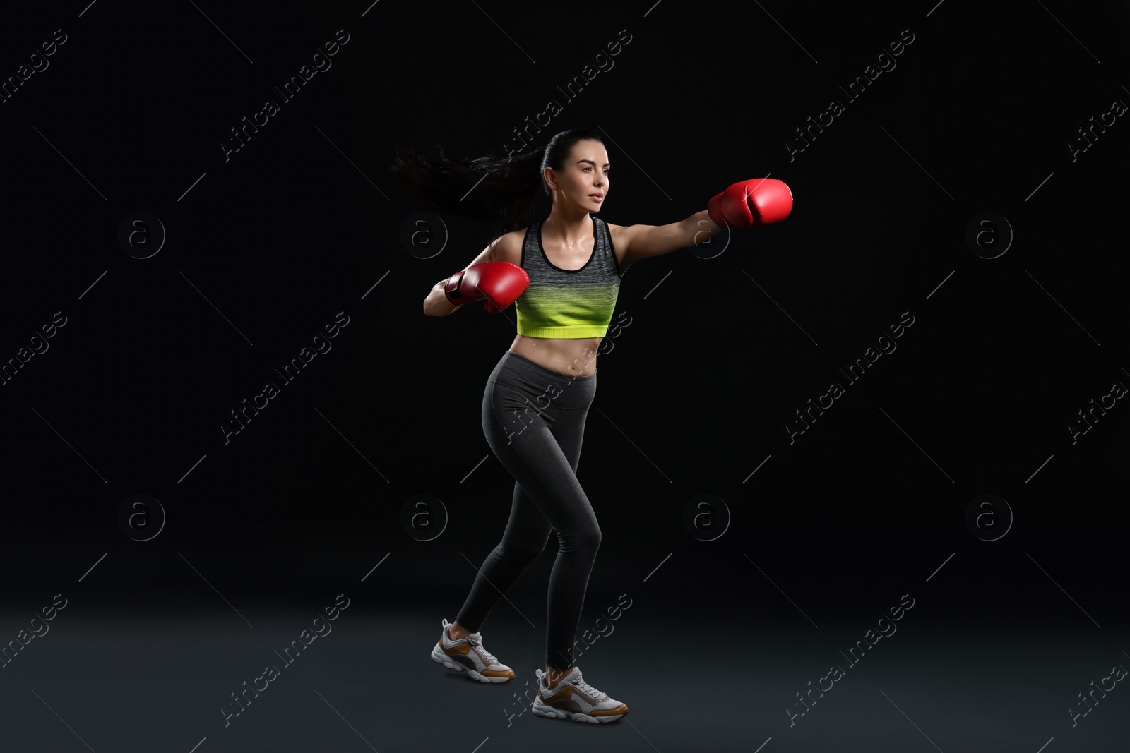 Photo of Beautiful woman in boxing gloves training on black background