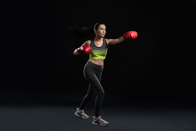 Photo of Beautiful woman in boxing gloves training on black background