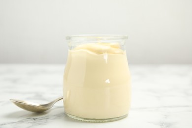 Photo of Jar of delicious mayonnaise and spoon on white marble table