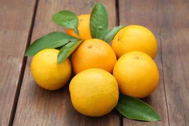 Photo of Many ripe oranges and green leaves on wooden table