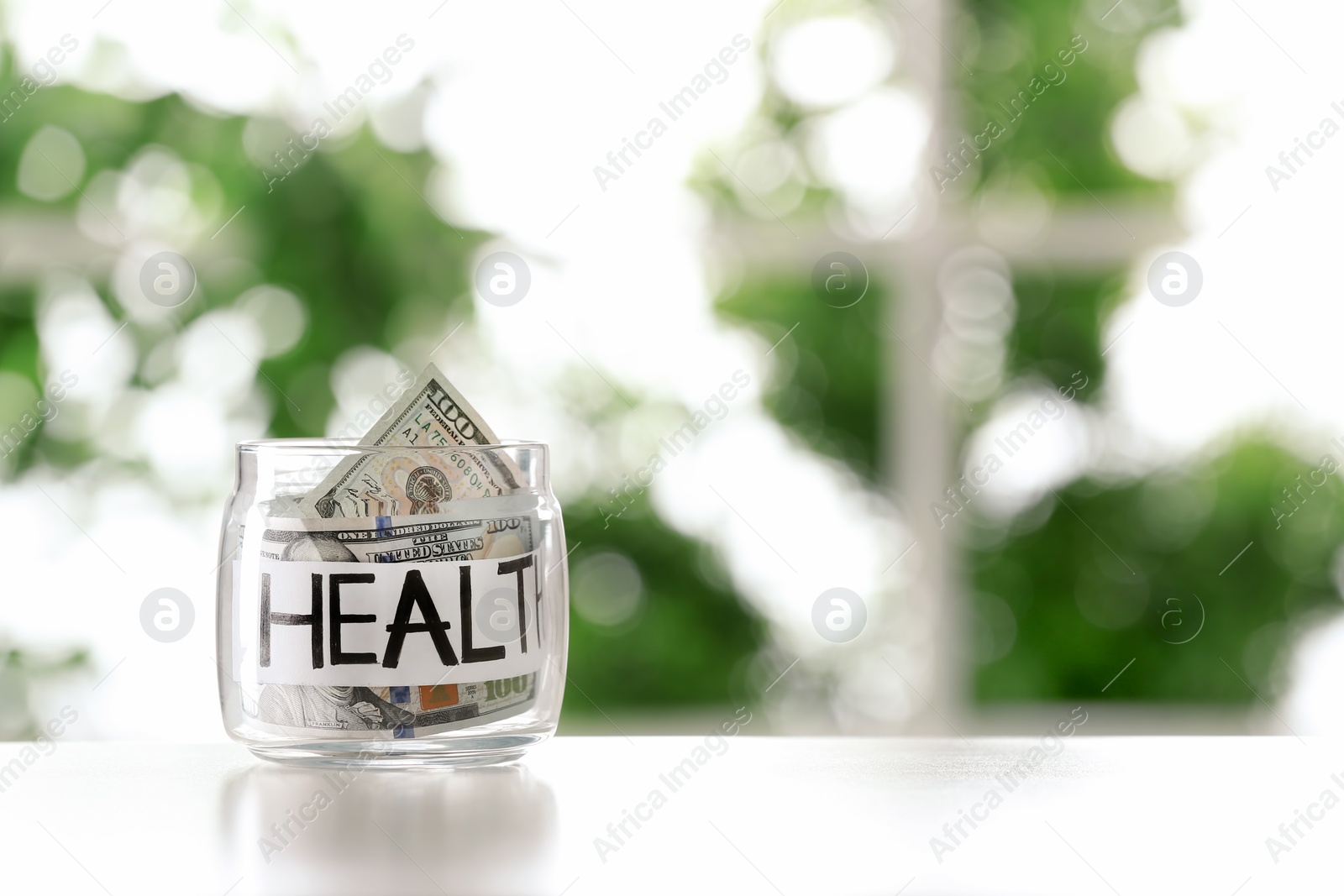 Photo of Glass jar with money and word HEALTH on table against blurred background, space for text