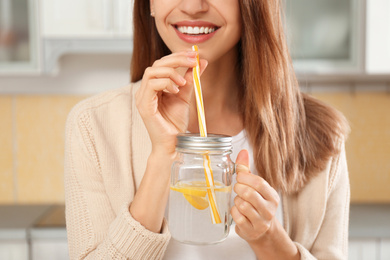Photo of Young woman drinking lemon water in kitchen, closeup
