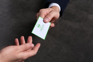 Man giving medical business card to woman on dark background, closeup. Nephrology service