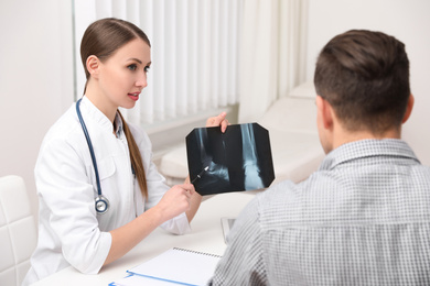 Photo of Orthopedist showing X-ray picture to patient at table in clinic
