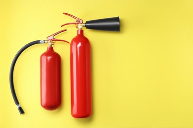 Photo of Fire extinguishers on yellow background, flat lay. Space for text