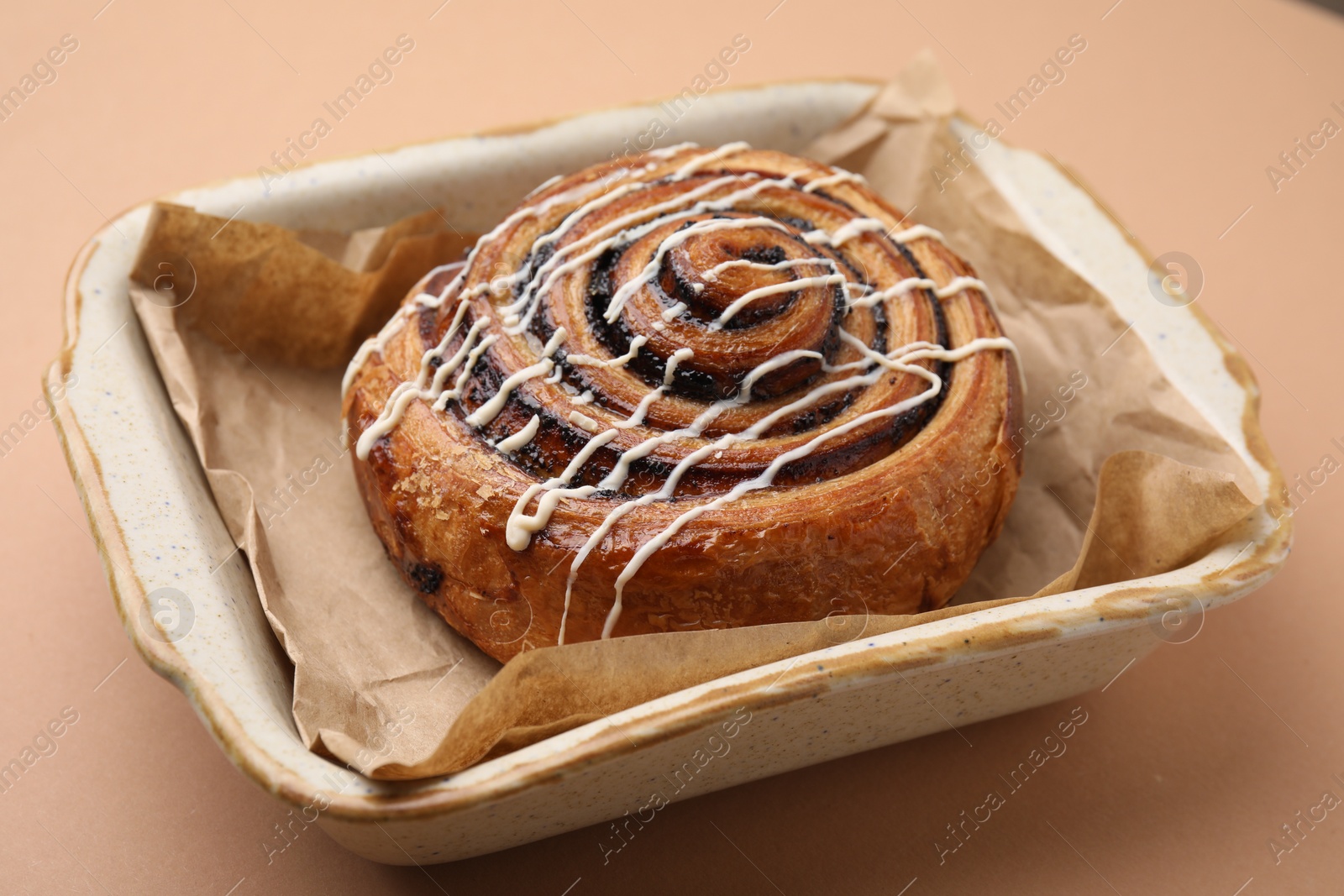 Photo of Delicious roll with topping and poppy seeds on beige table, closeup. Sweet bun