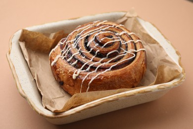 Delicious roll with topping and poppy seeds on beige table, closeup. Sweet bun