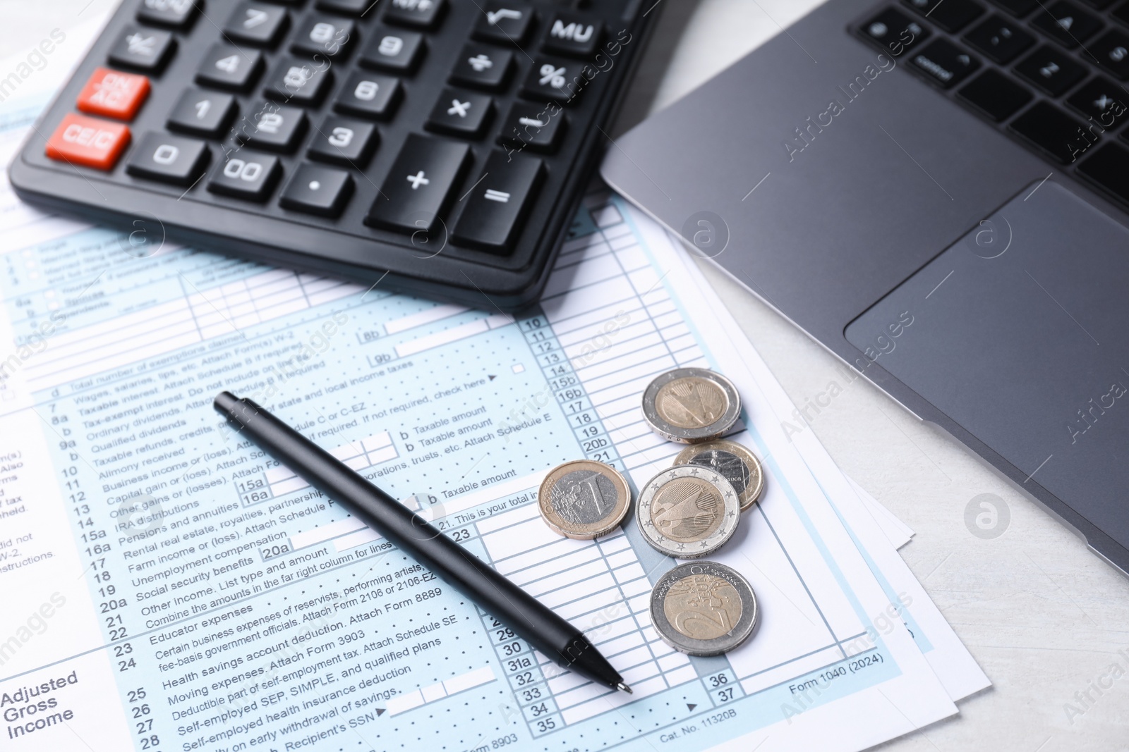 Photo of Tax forms, coins, pen, calculator and laptop on light grey table, closeup