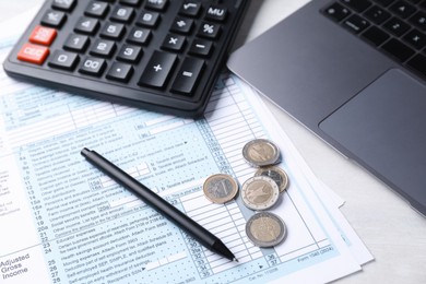 Tax forms, coins, pen, calculator and laptop on light grey table, closeup