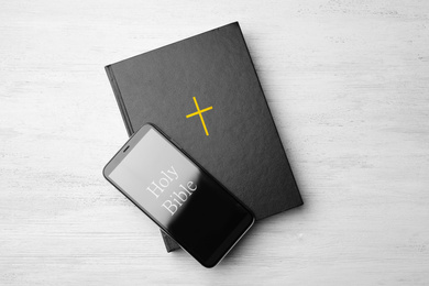 Photo of Bible and phone on white wooden background, top view. Religious audiobook