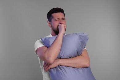 Sleepy man with pillow yawning on grey background. Insomnia problem
