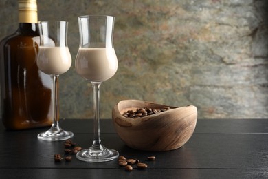 Photo of Coffee cream liqueur in glasses, bottle and beans on black wooden table