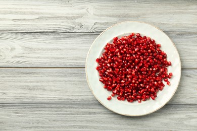 Photo of Tasty ripe pomegranate grains on light wooden table, top view. Space for text