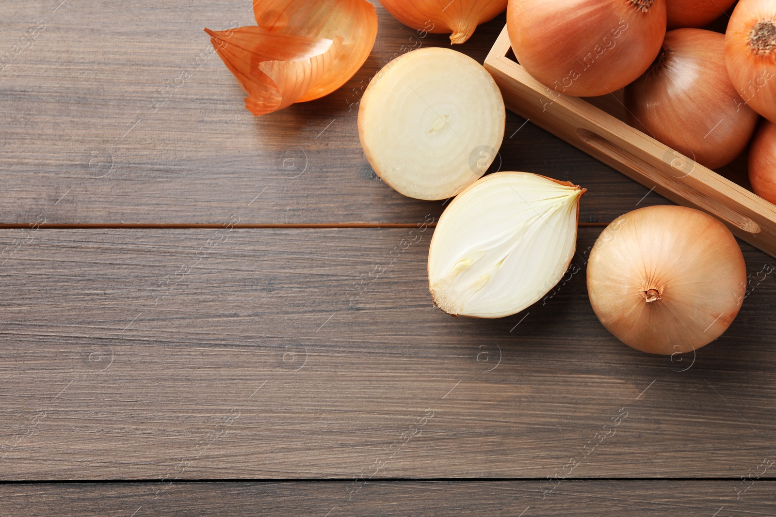 Photo of Whole and cut onions on wooden table, flat lay. Space for text
