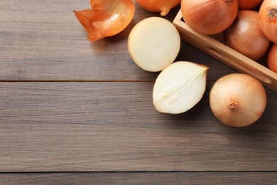 Whole and cut onions on wooden table, flat lay. Space for text