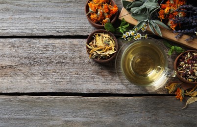 Photo of Glass cup of aromatic freshly brewed tea near different dry herbs on wooden table, flat lay. Space for text