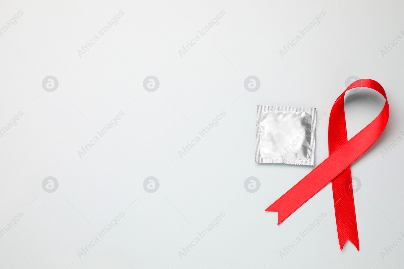 Photo of Red ribbon and condom on white background, top view. AIDS disease awareness