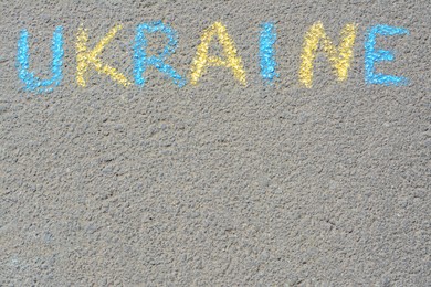 Photo of Word Ukraine written with blue and yellow chalks on asphalt outdoors, top view. Space for text