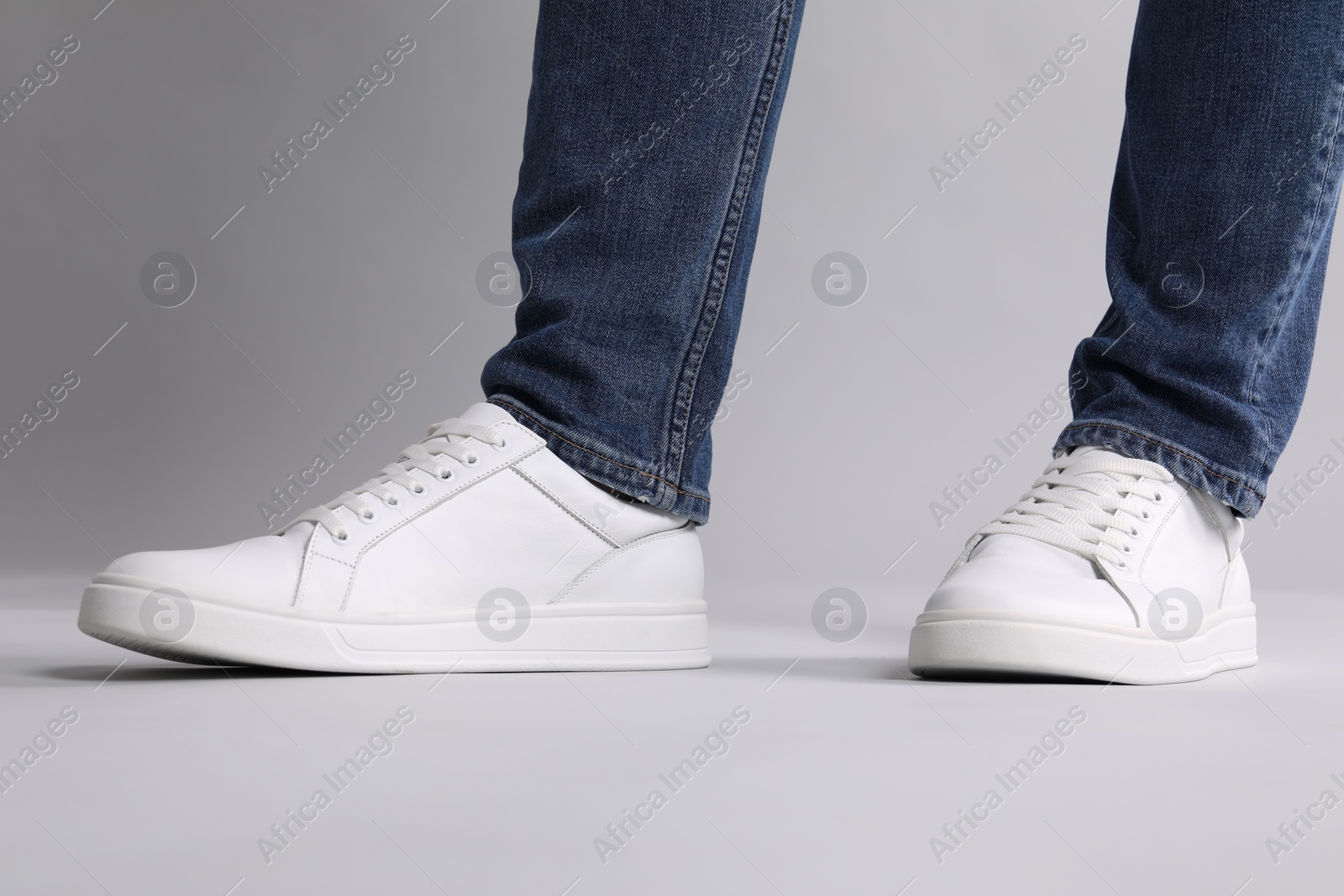 Photo of Man wearing stylish white sneakers on grey background, closeup