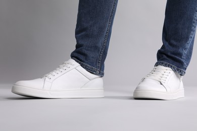 Photo of Man wearing stylish white sneakers on grey background, closeup