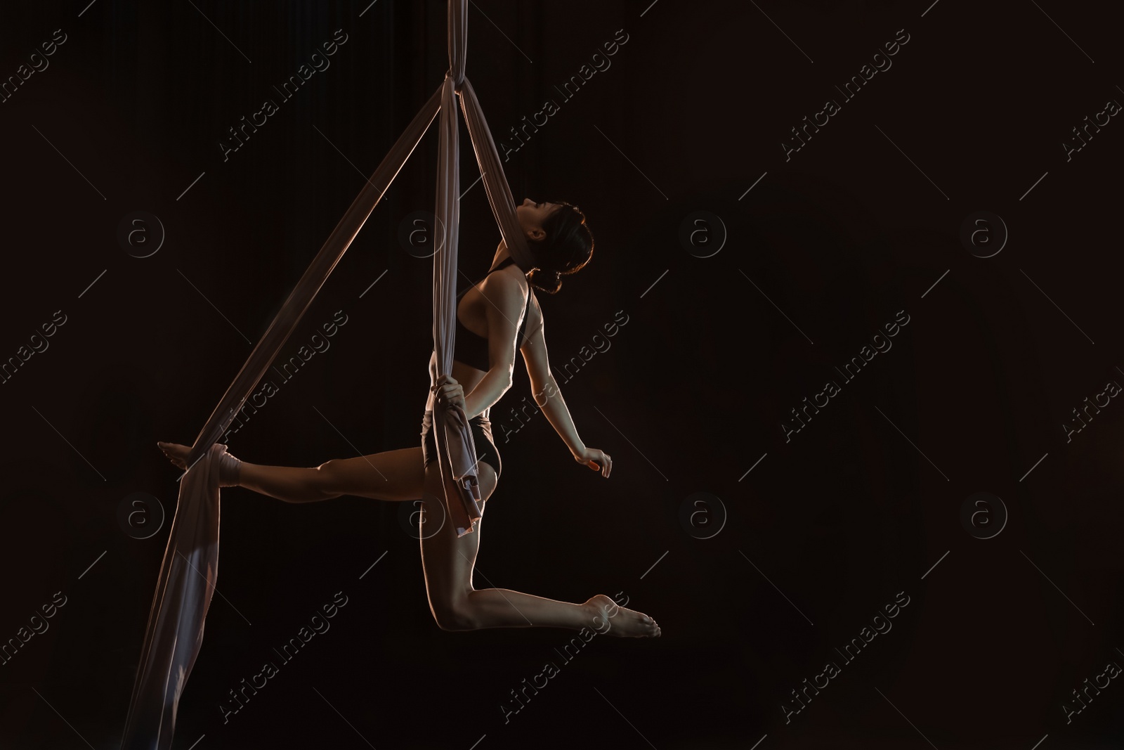 Photo of Young woman performing acrobatic element on aerial silk indoors. Space for text