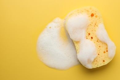 Sponge with foam on yellow background, top view. Space for text