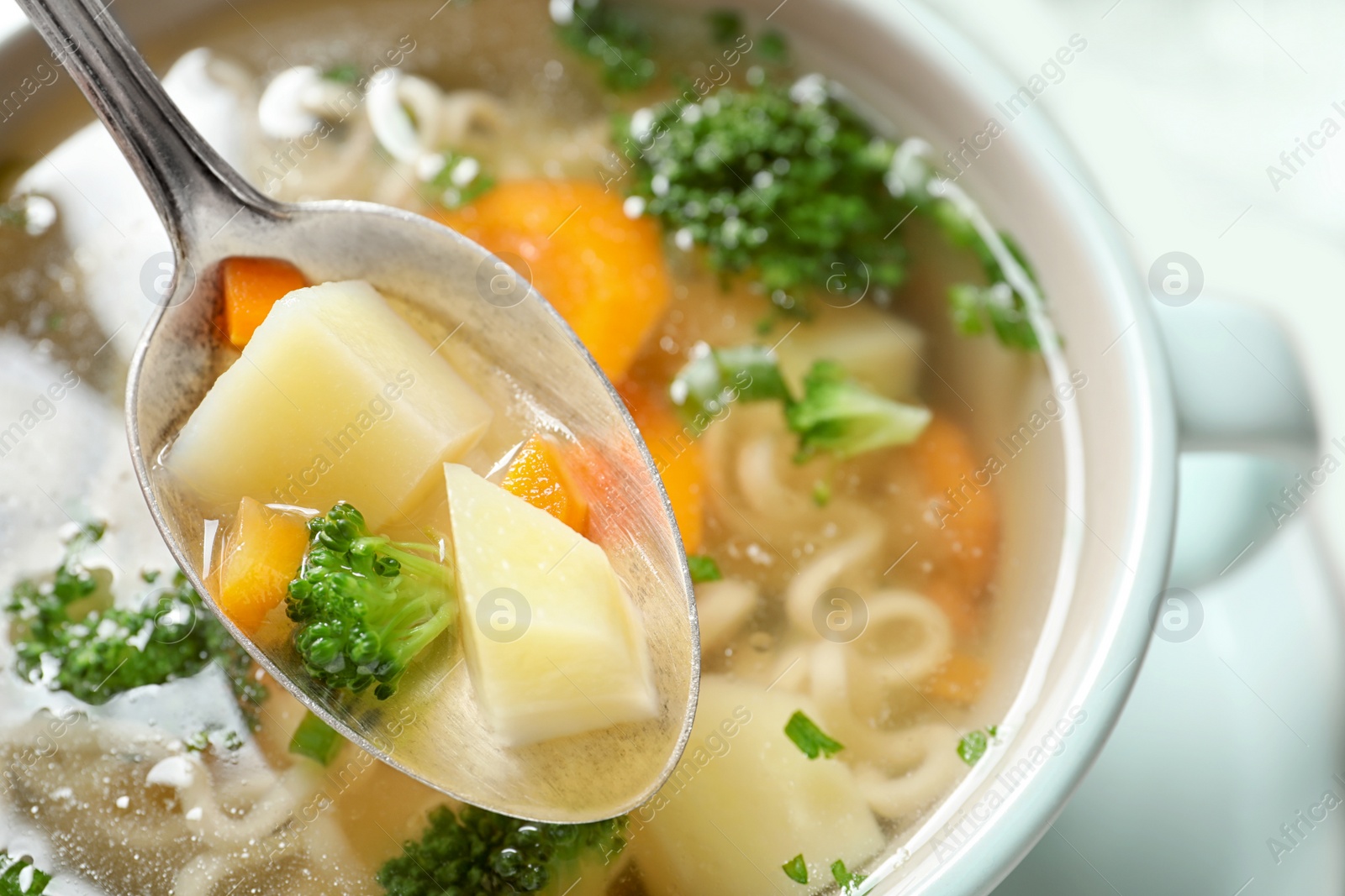 Photo of Spoon of fresh homemade vegetable soup over full dish on table, closeup