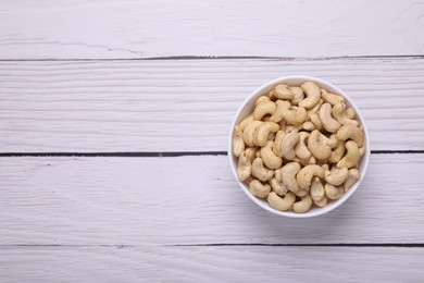 Tasty cashew nuts in bowl on white wooden table, top view. Space for text