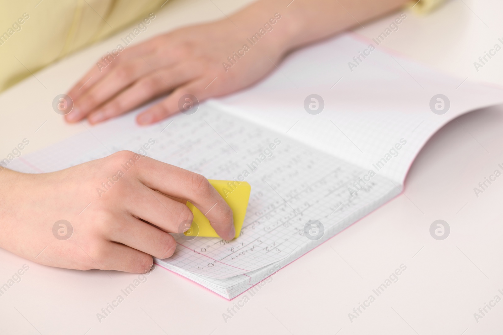 Photo of Girl erasing mistake in her notebook at white desk, closeup