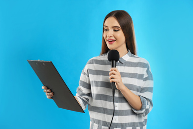 Young female journalist with microphone and clipboard on blue background