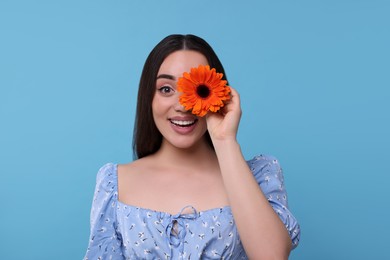 Photo of Beautiful woman with spring flower in hand on light blue background