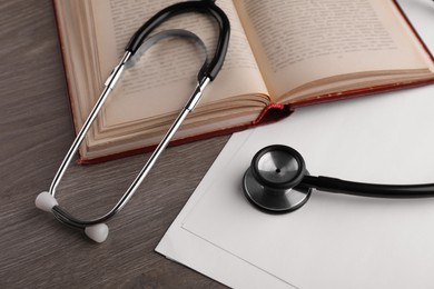 Photo of Book, stethoscope and sheets of paper on wooden table. Medical education