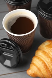 Photo of Coffee to go. Paper cups with tasty drink and croissant on grey wooden table, closeup