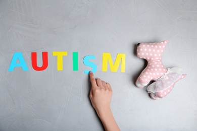 Woman pointing at word AUTISM and toy dog on grey background, top view