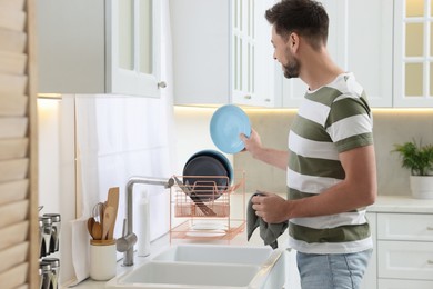 Man putting clean plate on drying rack in kitchen