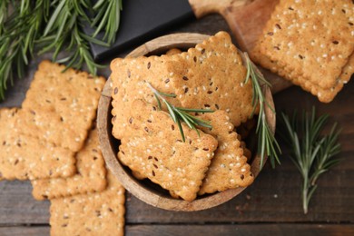 Photo of Cereal crackers with flax, sesame seeds and rosemary on wooden table, flat lay