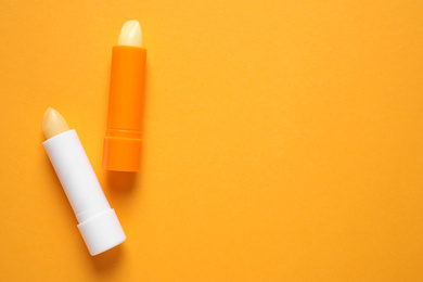 Photo of Hygienic lipsticks on orange background, flat lay. Space for text