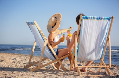 Young couple with cocktails in beach chairs at seacoast