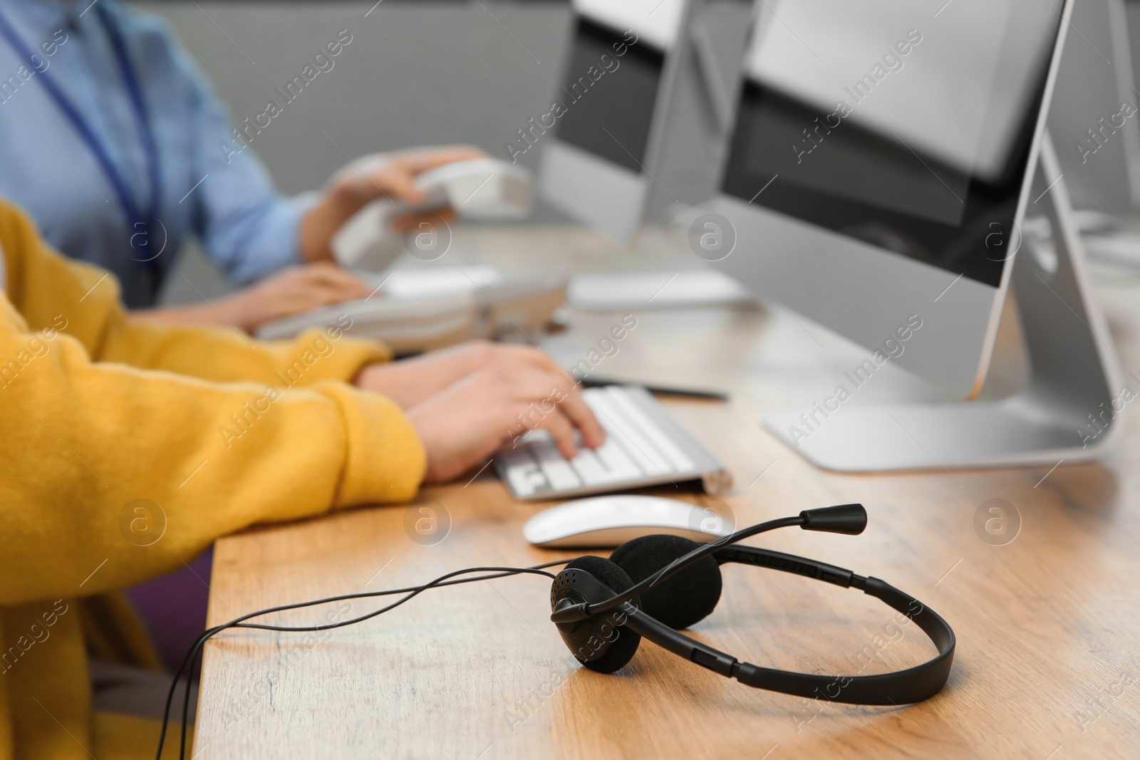 Photo of Technical support operators working at table in office, focus on headset