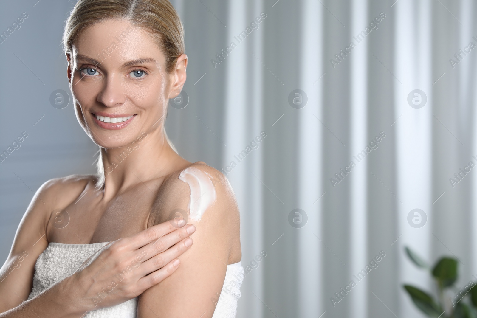 Photo of Happy woman applying body cream onto shoulder indoors, space for text