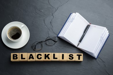 Photo of Wooden cubes with word Blacklist, cup of coffee and office stationery on slate table, flat lay