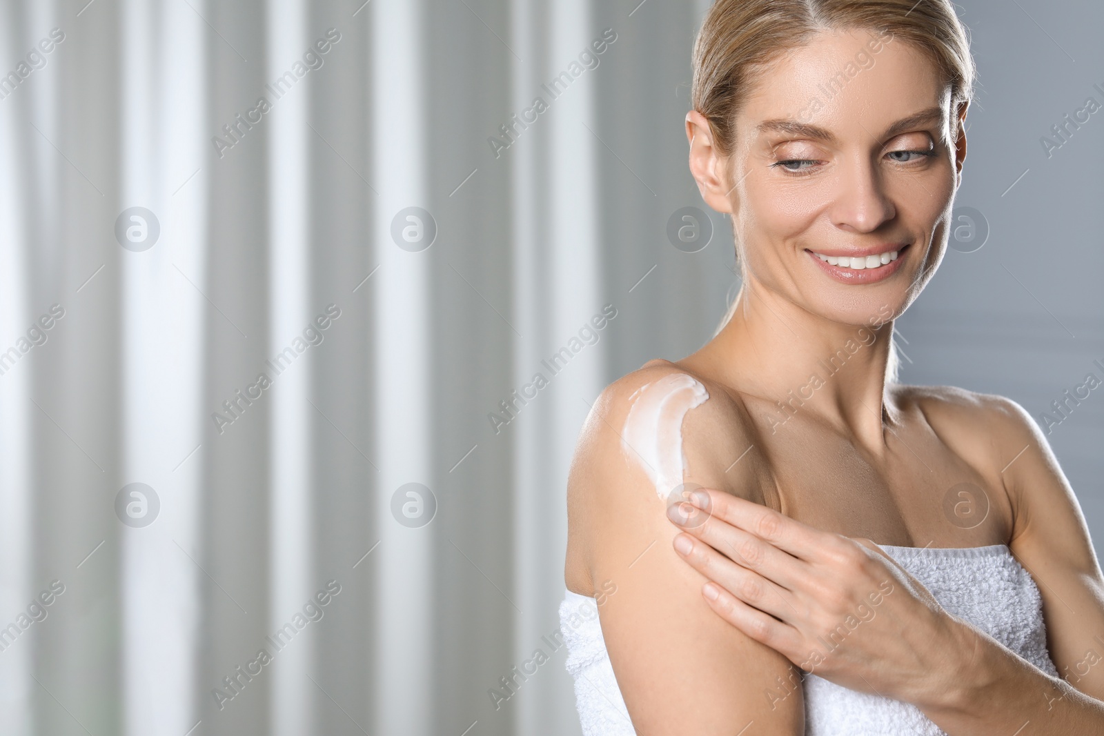 Photo of Happy woman applying body cream onto shoulder indoors, space for text