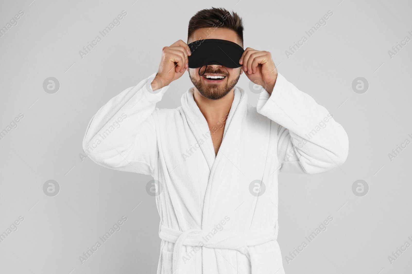 Photo of Young man in bathrobe and eye sleeping mask on light grey background