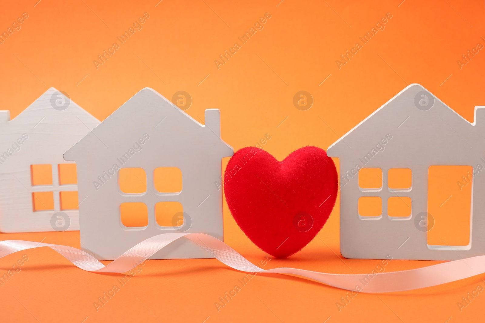 Photo of Long-distance relationship concept. Decorative heart between white house models and ribbon on orange background