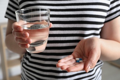 Woman with glass of water and pills on blurred background, closeup