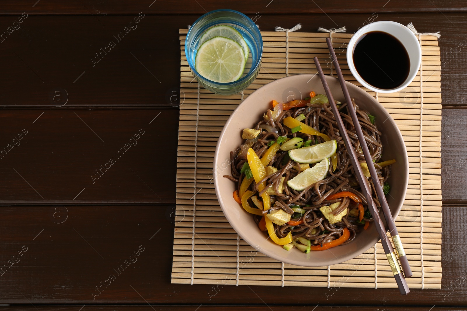 Photo of Stir-fry. Delicious cooked noodles with chicken and vegetables in bowl served on wooden table, flat lay. Space for text