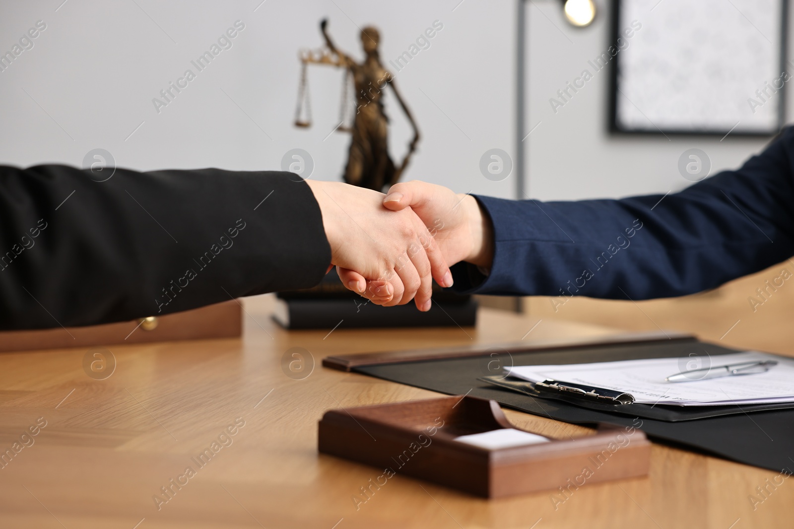 Photo of Notary shaking hands with client at wooden table in office, closeup