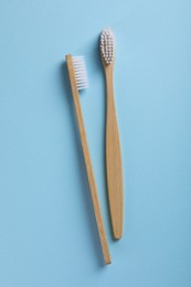 Photo of Bamboo toothbrushes on light blue background, flat lay