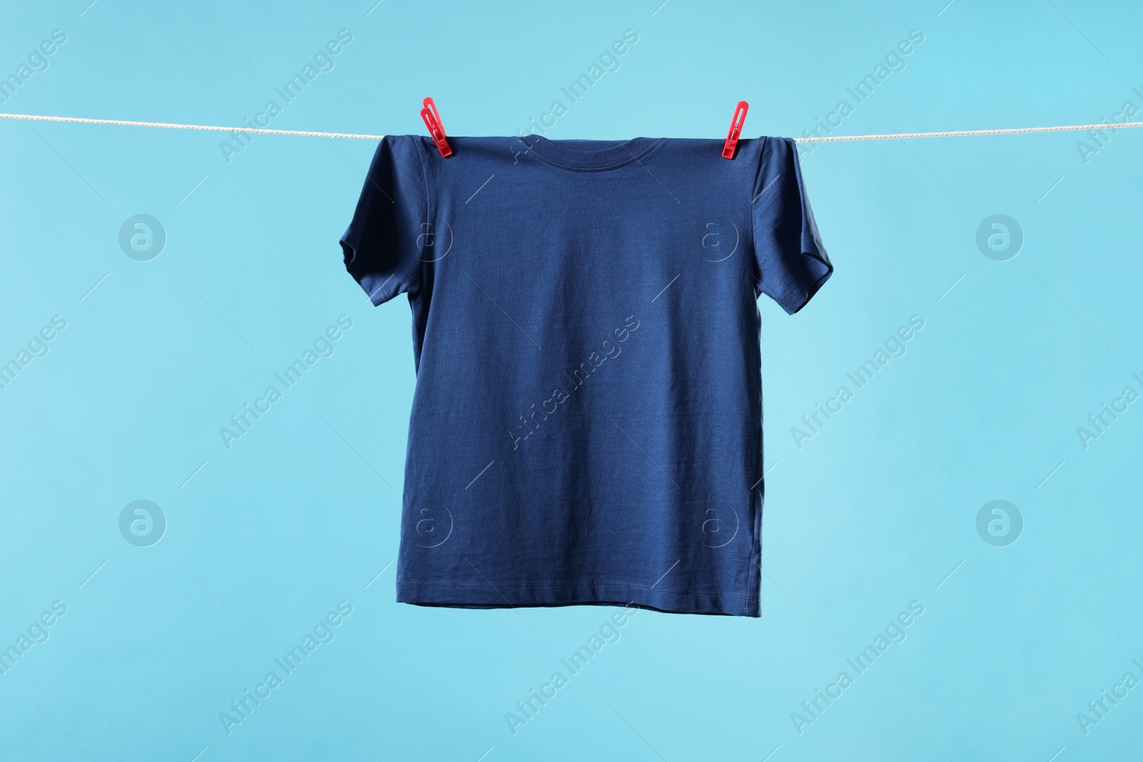 Photo of One t-shirt drying on washing line against light blue background. Space for text