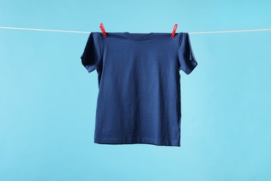 Photo of One t-shirt drying on washing line against light blue background. Space for text